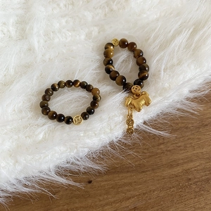 Close-up of tiger eye stone bead rings with gold coin charms on a soft plush surface