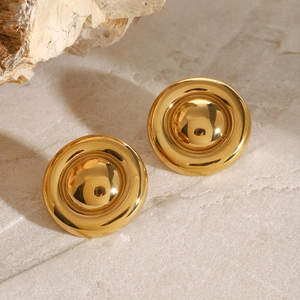 Close-up of golden round domed stud earrings on a textured stone surface