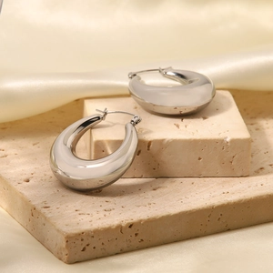 Detail of silver water-drop hoop earrings on beige stone with soft satin fabric