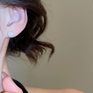 Close-up of elegant round white pearl stud earring worn on model's earlobe