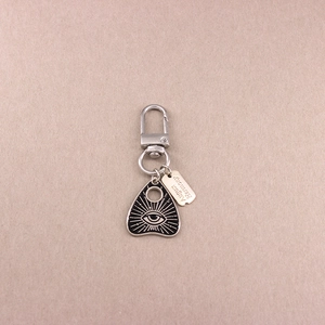 Détail d'un porte-clés en alliage argenté avec pendentif planchette noire et motif d'œil
