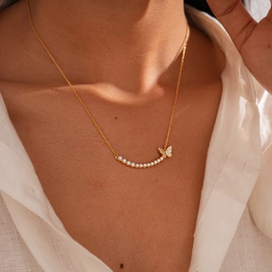 Close-up of 18k gold plated butterfly pendant with zircons and pearls on necklace