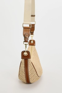 Close-up of beige woven crossbody bag with brown leather strap and gold metal hardware