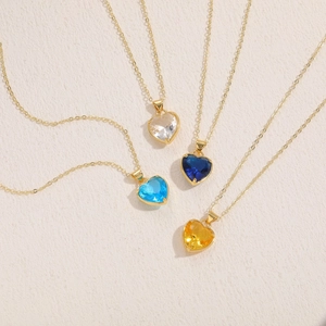 Classic glass heart pendant necklace in four colors with gold chain on beige background