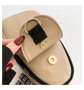 Dettaglio della fibbia magnetica dorata e cinturino nero su borsa in pelle beige