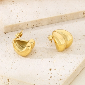 Detailed close-up of golden irregular heart-shaped earrings on a beige stone surface
