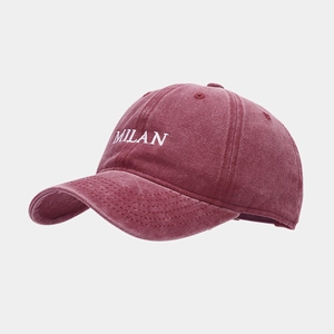 Detailed close-up of white MILAN embroidery on a washed burgundy cotton baseball cap