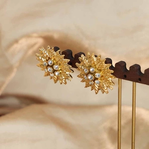 Elegant gold-plated titanium sunflower earrings with sparkling cubic zirconia on wood stand