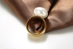 Detailed close-up of golden hammered ring featuring a large white pearl on silk fabric