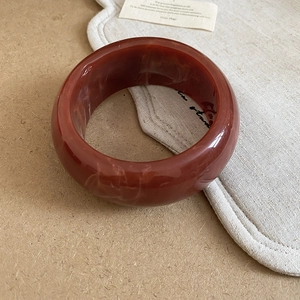 Detail of red-brown resin bangle with white marble texture on a soft fabric background