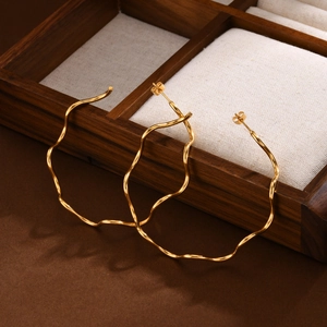 Detailed view of wavy 18K gold hoop earrings with polished finish on a wooden jewelry box