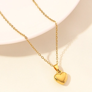 Close-up of a polished gold heart pendant necklace on a textured white ceramic plate