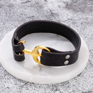 Detail of black braided leather bracelet featuring a golden anchor shackle clasp