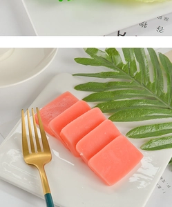 Detailed view of rectangular pink simulation food cubes on a white plate with cutlery