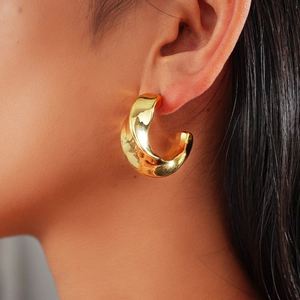 Gros plan de boucles d'oreilles créoles C dorées avec finition miroir métallique