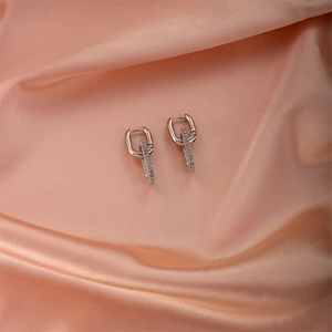 Macro shot of silver U-shaped earrings with zircon geometric pendants on pink silk fabric