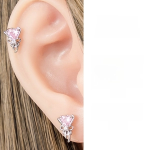 Detail of pink heart zircon stud earrings with silver bow design on female ear