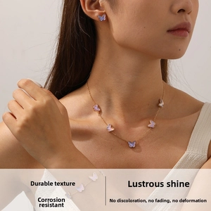 Detail of pink butterfly necklace and earrings set worn by model with gold chain and charms
