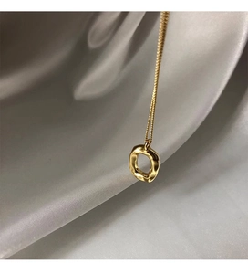 Detail of organic oval golden pendant with textured finish on silk fabric background