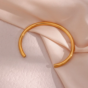 Detail view of a 18K gold-plated stainless steel open bangle on elegant silk fabric