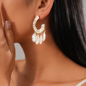 Détail de boucles d'oreilles dorées en C avec zircons et franges nacrées sur un mannequin