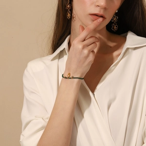 Close-up of a model wearing a beaded green bracelet and gold hollow flower earrings