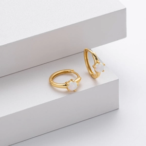 Macro detail of gold hoop earrings set with round white opal stones on white background