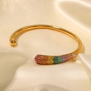 Detailed close-up of a 18K gold-plated open bangle with rainbow rhinestones on silk