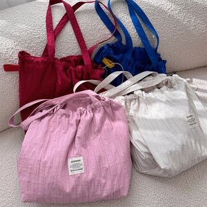 Close-up of pleated tote bags in pink, white, red, and blue on soft fabric background