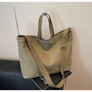 Close-up of olive green canvas tote bag with adjustable strap resting on a leather chair