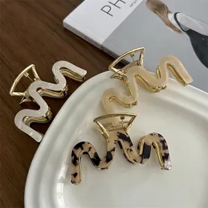 Three wave-shaped acetate hair claws in white, yellow, and tortoiseshell on a ceramic plate