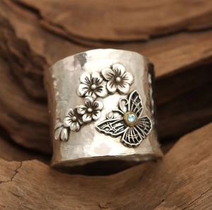 Close-up of a silver floral ring featuring a blue gemstone and hammered texture
