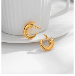 Close-up of chunky gold-plated C-shape hoop earrings on a white textured ceramic cup