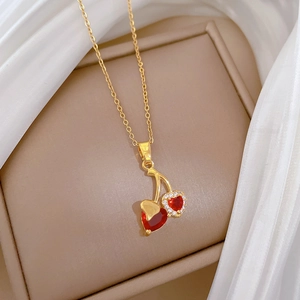 Close-up of gold cherry pendant with red heart gemstone and crystals on velvet box