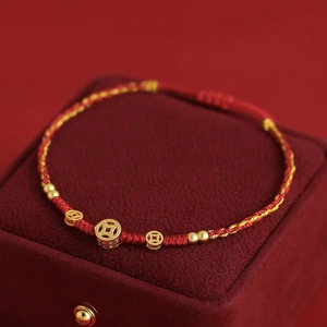 Détail d'un bracelet tressé en cordon rouge avec trois pièces d'or et fermoir réglable