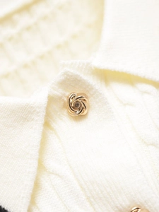 Close-up of golden spiral petal button on cream knit polo shirt with ribbed texture