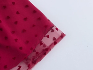 Gros plan sur le tissu en tulle rouge avec motifs cœurs floqués et détails de l'ourlet