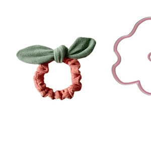 Pink suede ruffled scrunchie with green plush rabbit ear bow on a white background