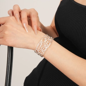 Gros plan d'un large bracelet manchette argenté ajouré porté avec une tenue élégante