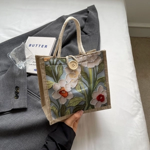 Close-up of linen floral handbag featuring woven handles and a wooden button detail
