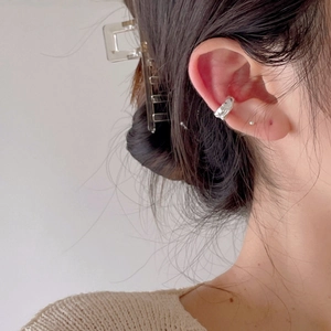 Detailed close-up of a silver irregular lava-style ear cuff worn on the earlobe