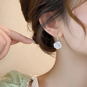 Close-up of elegant camellia earrings with white petals, gold edges and tiny rhinestones