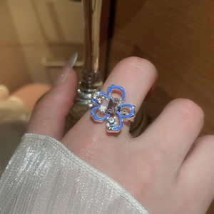 Primo piano di un anello a fiore in smalto blu con zirconi indossato su una mano in casa