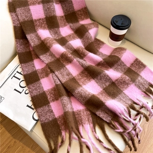 Detail of pink and brown plaid cashmere-like scarf with fringe on a cozy sofa