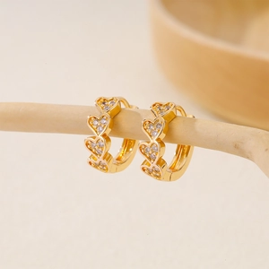 Elegant gold-plated heart-shaped huggie earrings with cubic zirconia on a wooden display