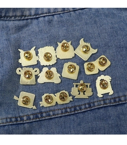 Detailed back view of twelve golden metal badges with butterfly clutches on denim fabric