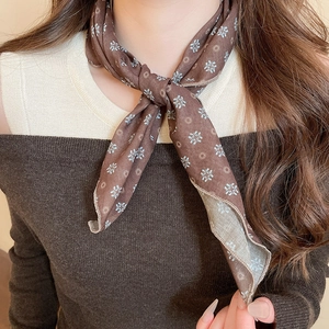 Close-up of a brown floral silk scarf tied in a bow around a model's neck