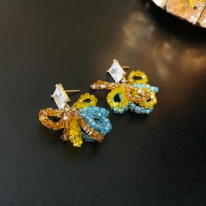 Macro detail of colorful beaded flower earrings with a diamond-like stud on black background