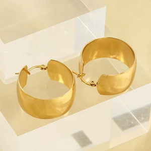 Gros plan de boucles d'oreilles créoles dorées larges avec finition métal poli