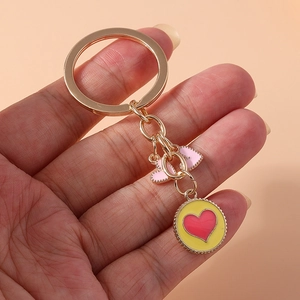 Detail of metal keychain with pink ribbon and yellow heart pendant held by hand